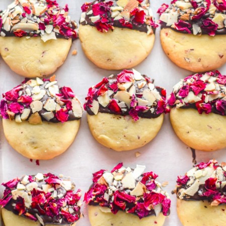 White shortbread cookies with chocolate dip on half and rose petals and white chocolate on top of the chocolate.