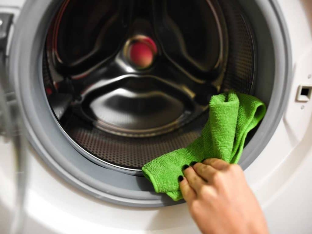 Hand using green microfiber cloth and vinegar cleaning solution wiping down the rubber on a washing machine.