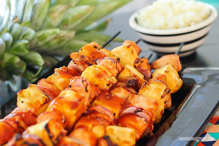 black rectangular plate with a stack of kabab skewers with pineapple, pineapple and onion with a glaze on top