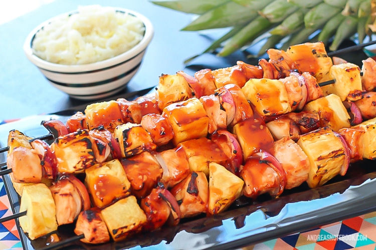 black rectangular plate with a stack of kabab skewers with pineapple, pineapple and onion with a glaze on top