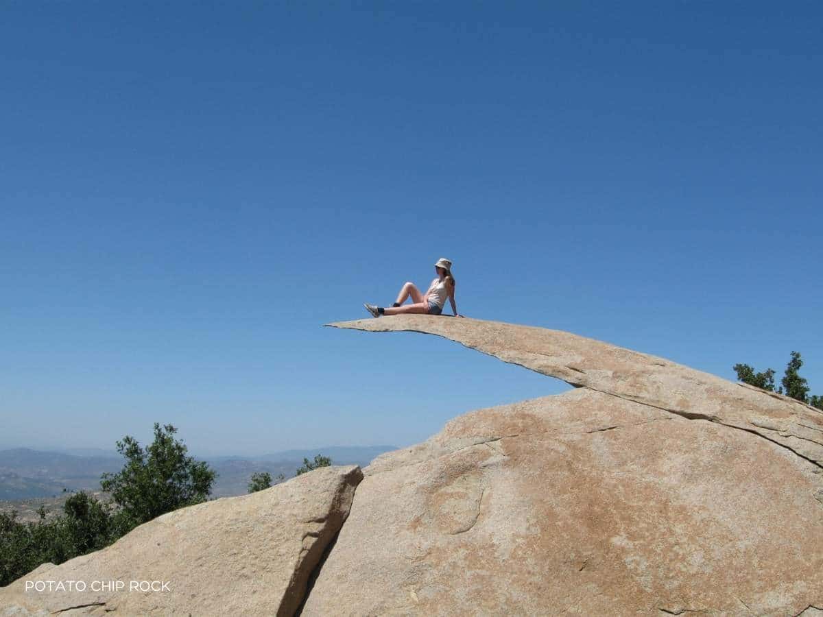 woman sitting on rock called potato chip rock because it looks like a sliver of a rock overhanging nothing