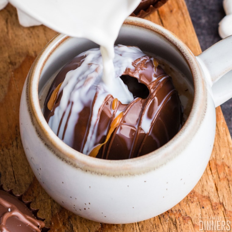 white mug with chocolate salted caramel hot chocolate bomb and milk being poured over the top, melting the top of the cocoa bomb.