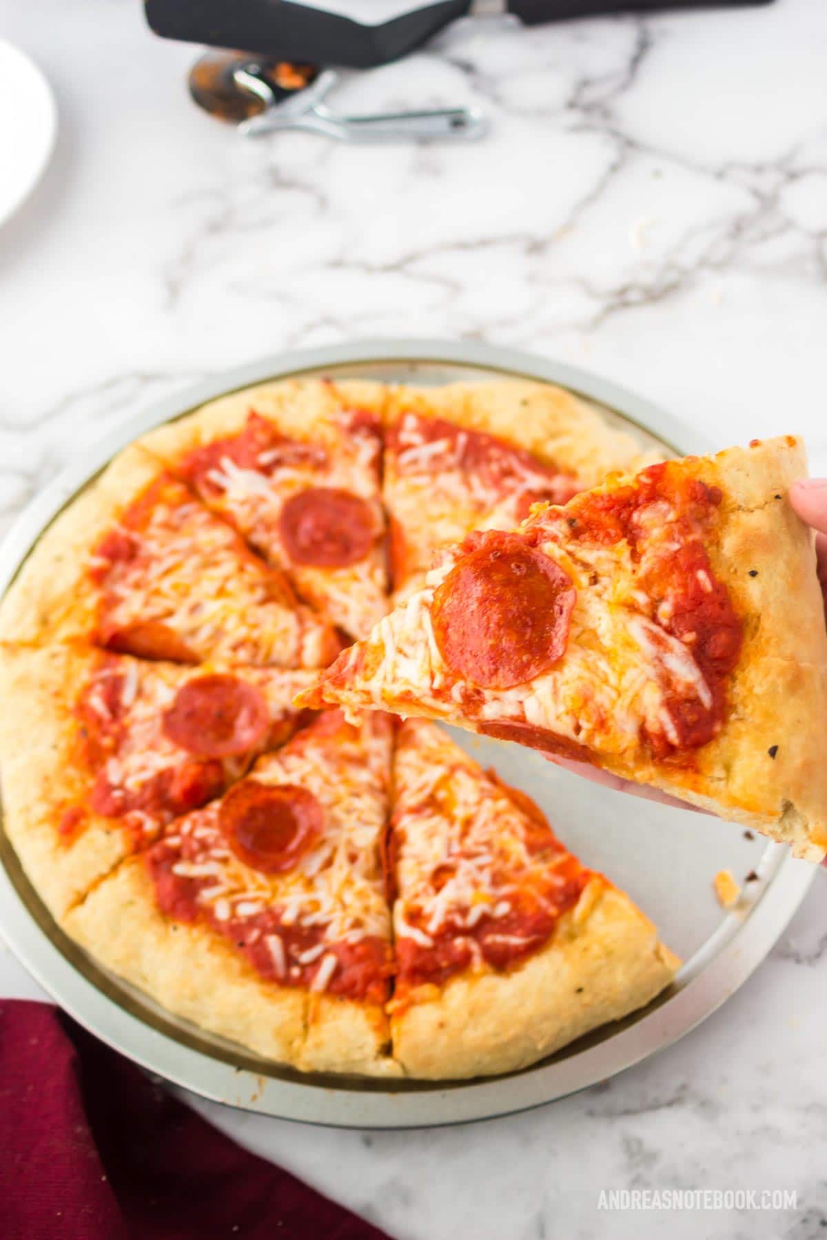 hand holding one slice of pizza up above a whole pizza crust - pan crust pizza