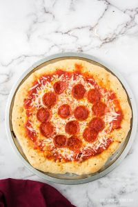 whole pepperoni pizza on white marble counter with subway tile background