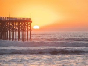 Best sunset! orange sunset behind Crystal Pier on Pacific Beach. Waves crash against pier and sun is almost below the horizon.
