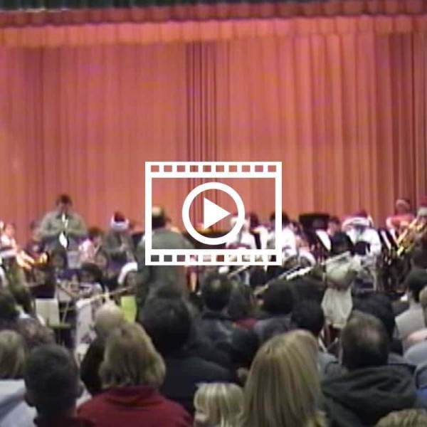 red stage curtain with band kids up front and backs of heads of people in the audience