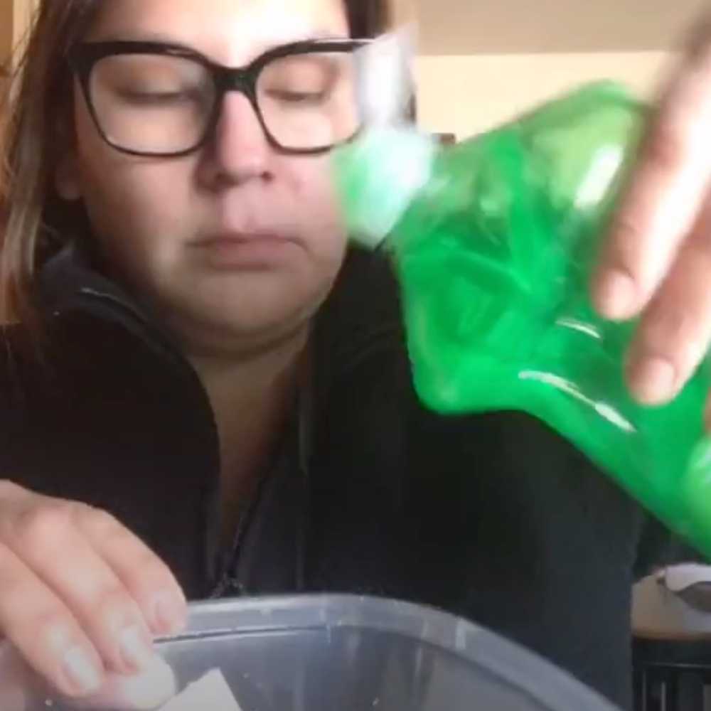 how to clean orange stains off plastic containers - White woman with black glasses and a black zip up fleece  uses kitchen tip DIY life hack to pour green dish soap into a plastic disposable container.