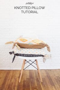 two pillows with knots on the corners sitting on white mid century modern chair. Hardwood floors with white background. Text says knotted pillow cover tutorial - learn how to make a pillow cover with zipper