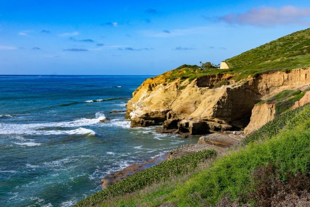 blue sky, green hills, brown cliffs and green ocean with waves