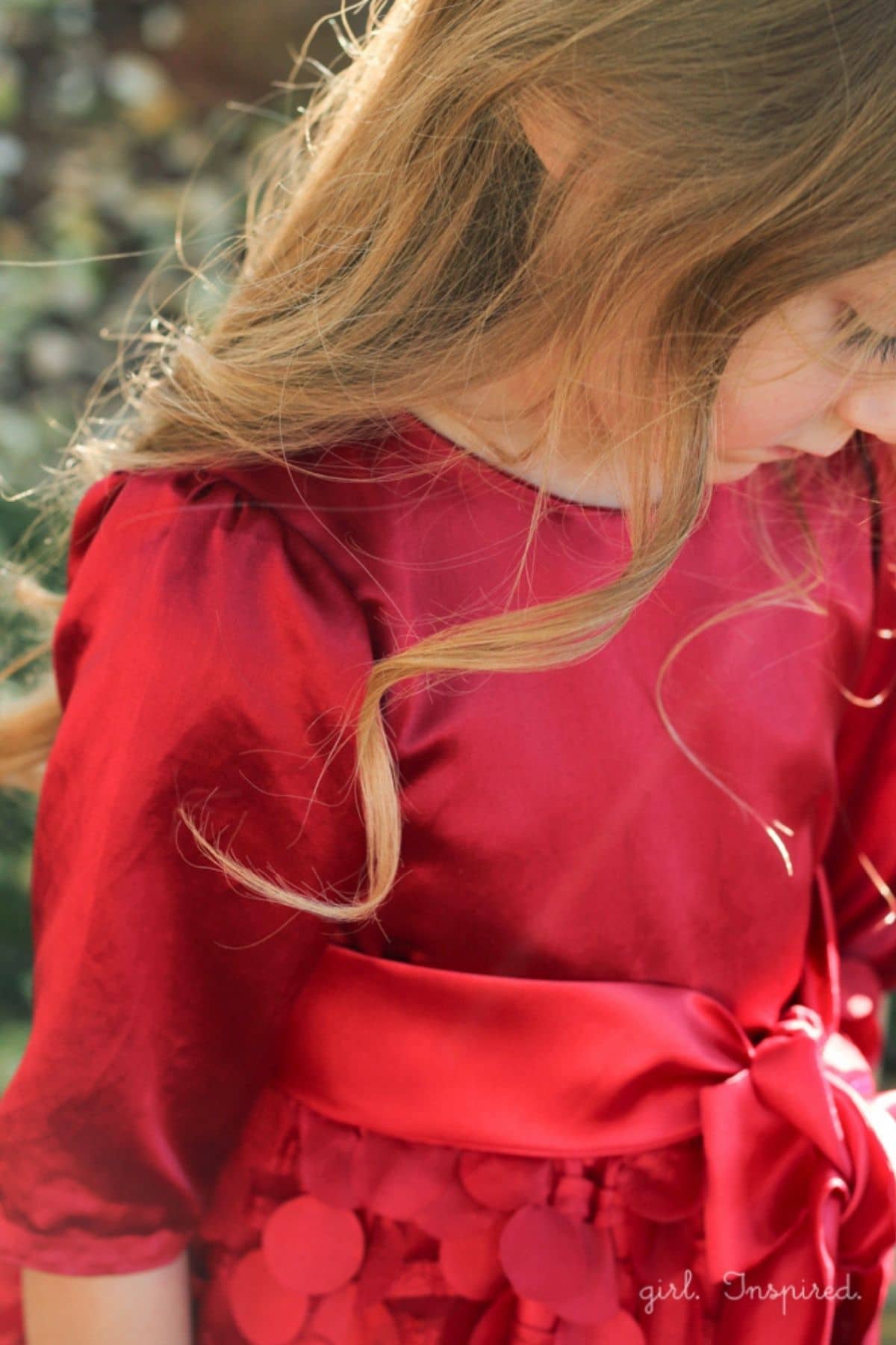 girl in red satin dress with puffed long sleeve. Image from her waist to mid face. Long brown hair.