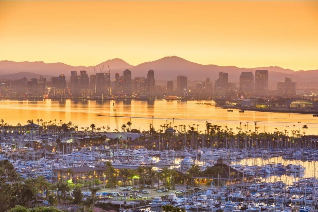 golden hour yellow sky over San Diego skyline with silhouette mountains in background. Harbor with sailboats in foreground