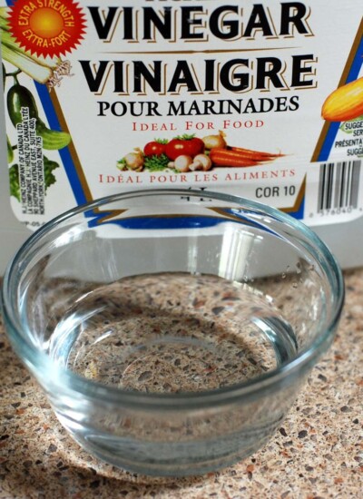 White vinegar in a glass bowl in front of a vinegar container.