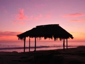 Where to watch the sunset in San Diego. Purple and pink sky makes for the best sunset with a thatched hut in silhouette at windansea beach in la Jolla north of San Diego