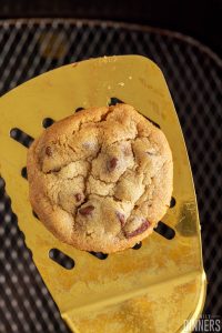 Chocolate chip cookie on a spatula over an air fryer basket.