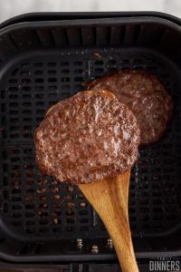 Hamburger patty on a spatula over an air fryer basket.