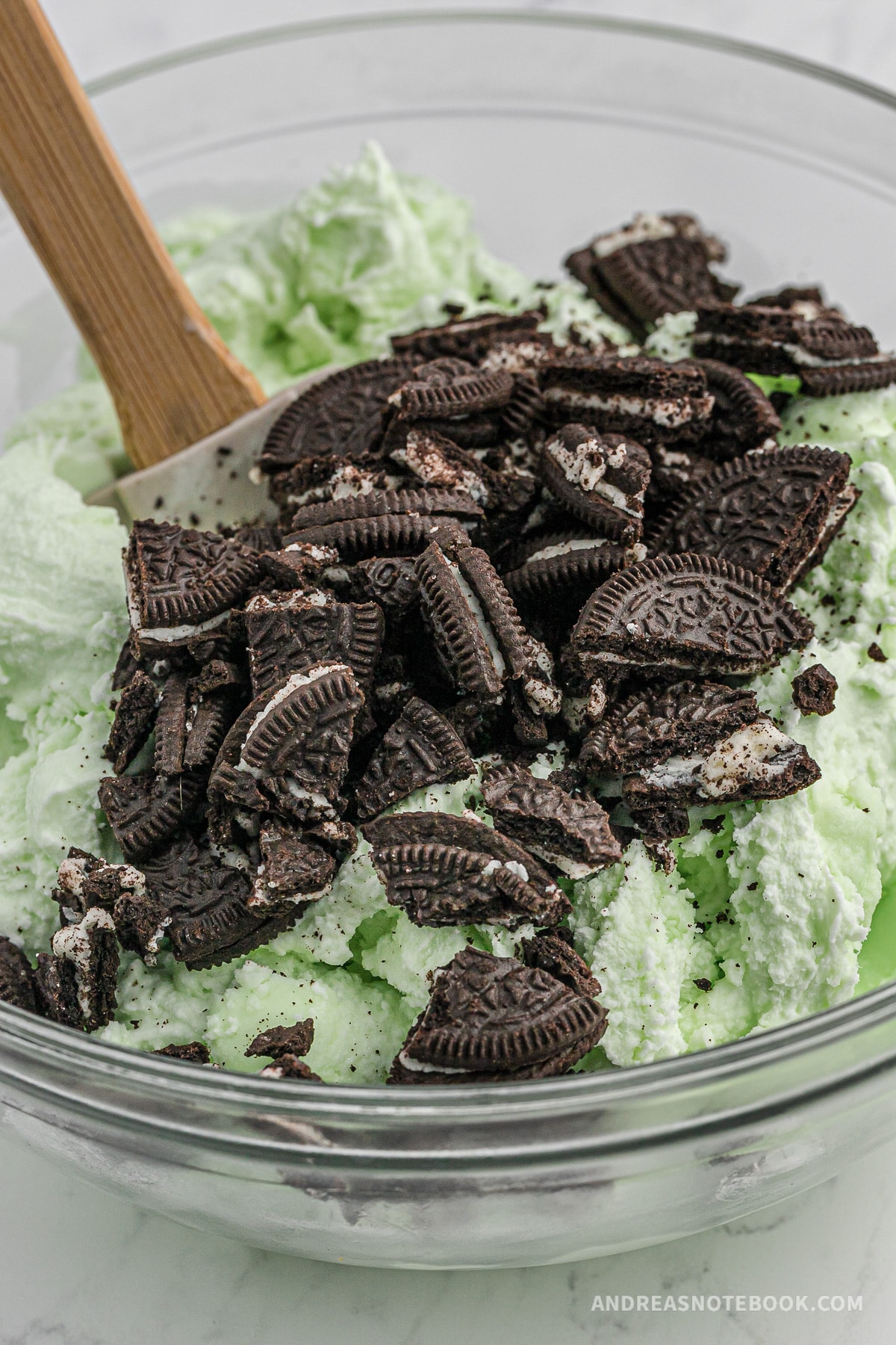 Oreo crumbles being stirred into mint ice cream.