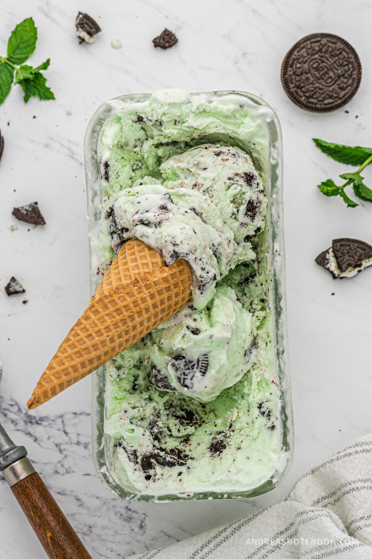 Ice cream cone with mint chocolate cookie ice cream in it on top of a dish of ice cream.