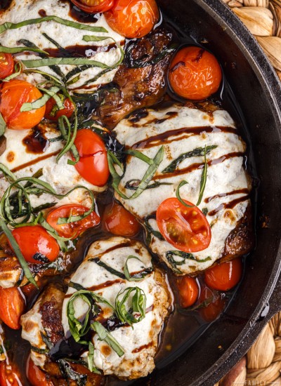 Caprese chicken thighs with cherry tomatoes in a skillet.