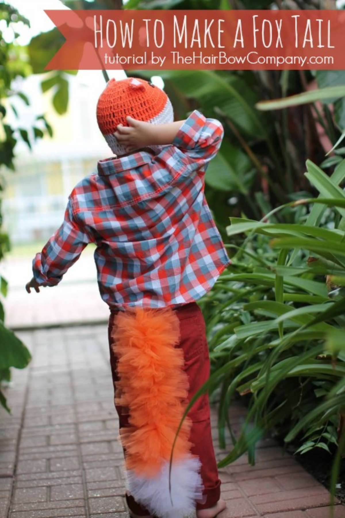 Boy in plaid shirt wearing orange and white tulle fox tail.