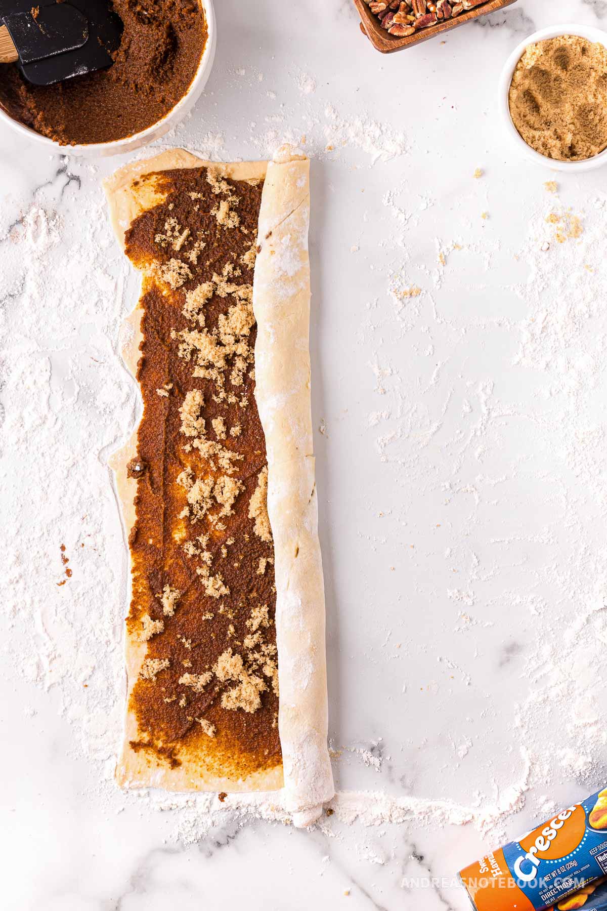 Dough being rolled up with cinnamon mixture and nuts inside.