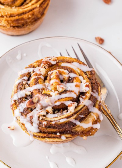 Delicious pumpkin cinnamon roll muffin with glaze drizzled on top.