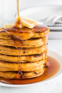 Stack of pumpkin pancakes with syrup pouring on top.