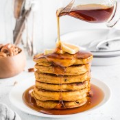 Syrup pouring over chocolate and pecan pumpkin pancakes pile.