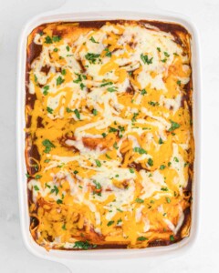 Baked enchiladas rojas in a pan with melted cheese on top.