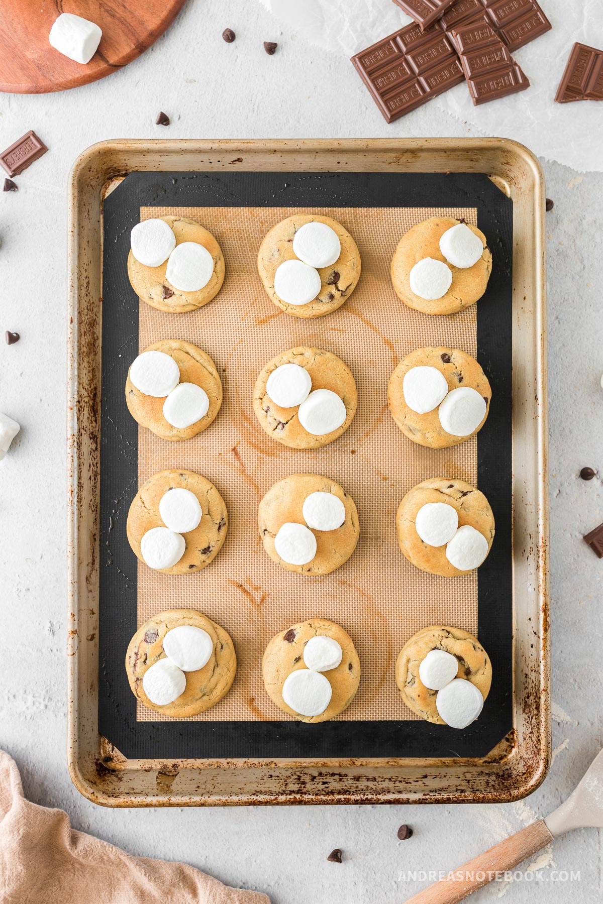 Cooked chocolate chip cookies on a tray with marshmallows on top.