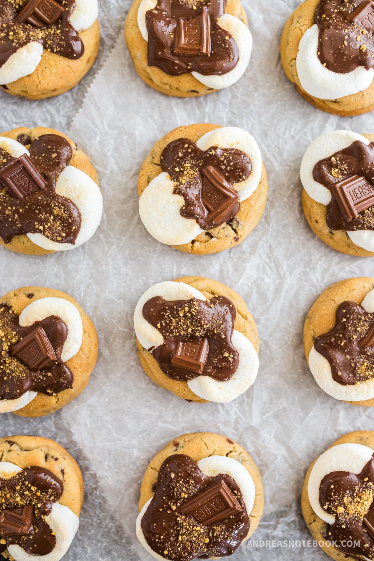 12 s'mores cookies on parchment. Chocolate chip cookie with marshmallow and melted chocolate on top.