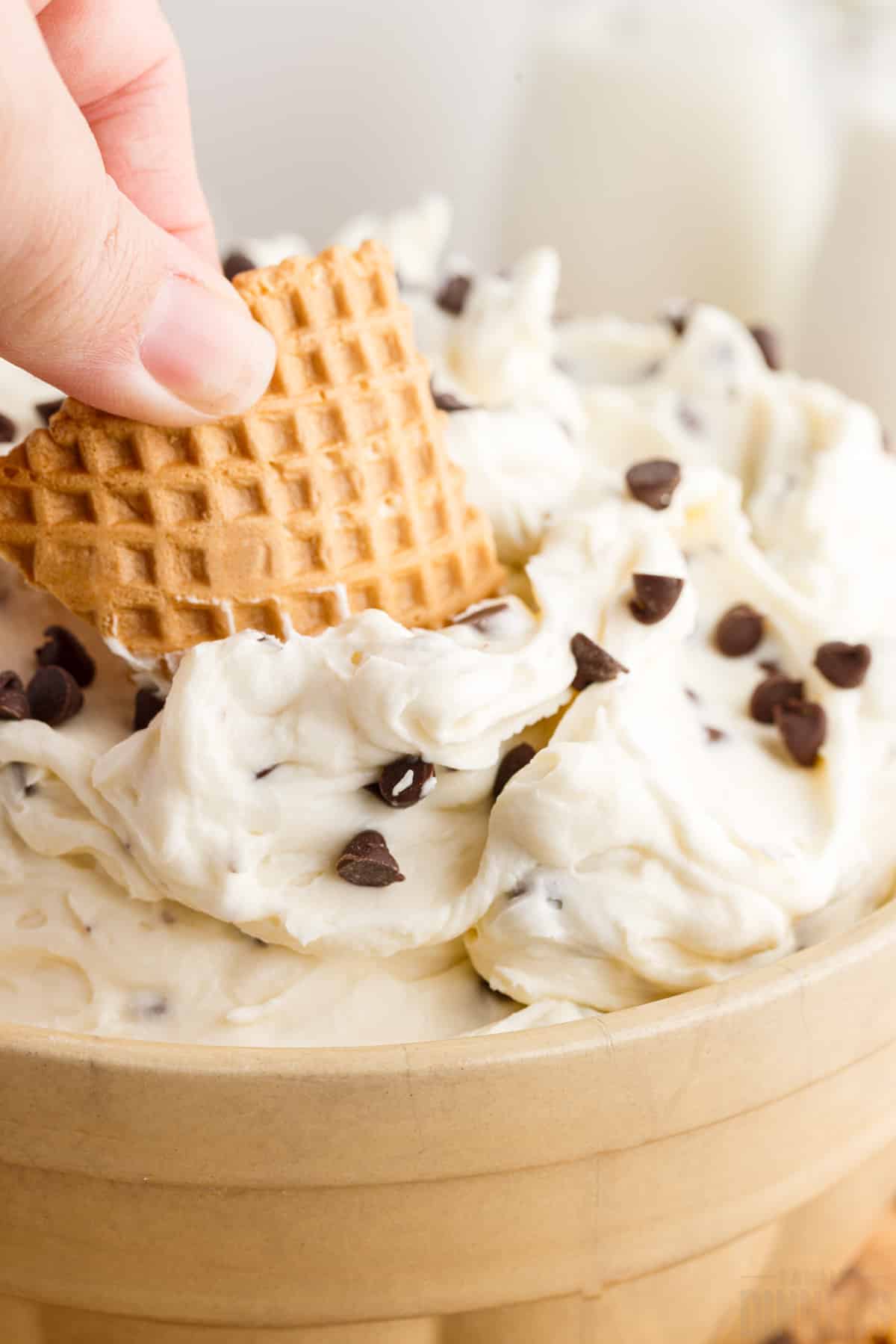 Piece of waffle cone being dipped into cannoli dip.