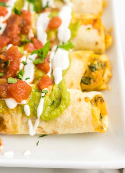 Platter of chicken taquitos garnished with guacamole, sour cream and salsa.