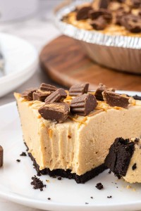 Bite out of a creaming looking peanut butter pie with reeces peanut butter cups on top.