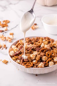 Spoon drizzling white chocolate over chex mix bowl.