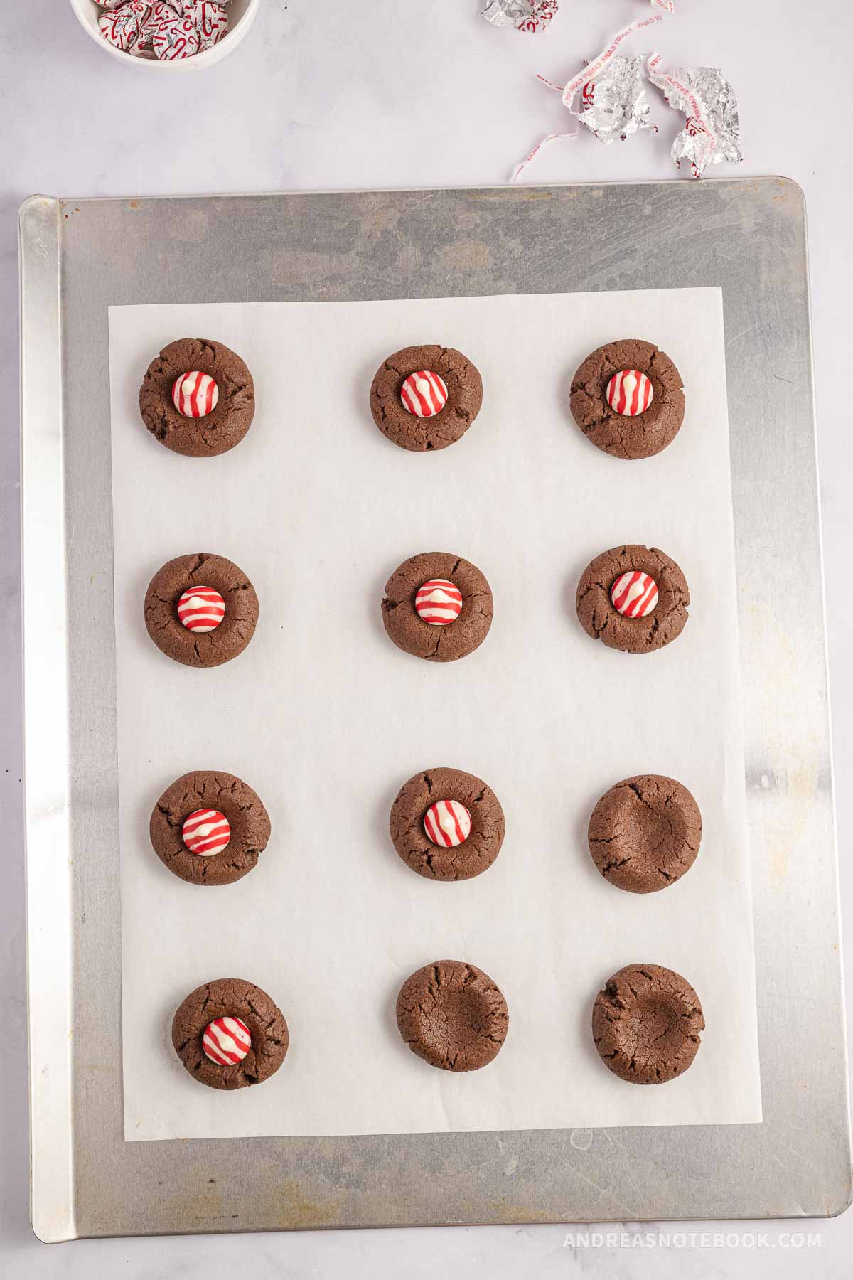 Red and white striped hershey kisses placed on chocolate cookies on baking sheet.