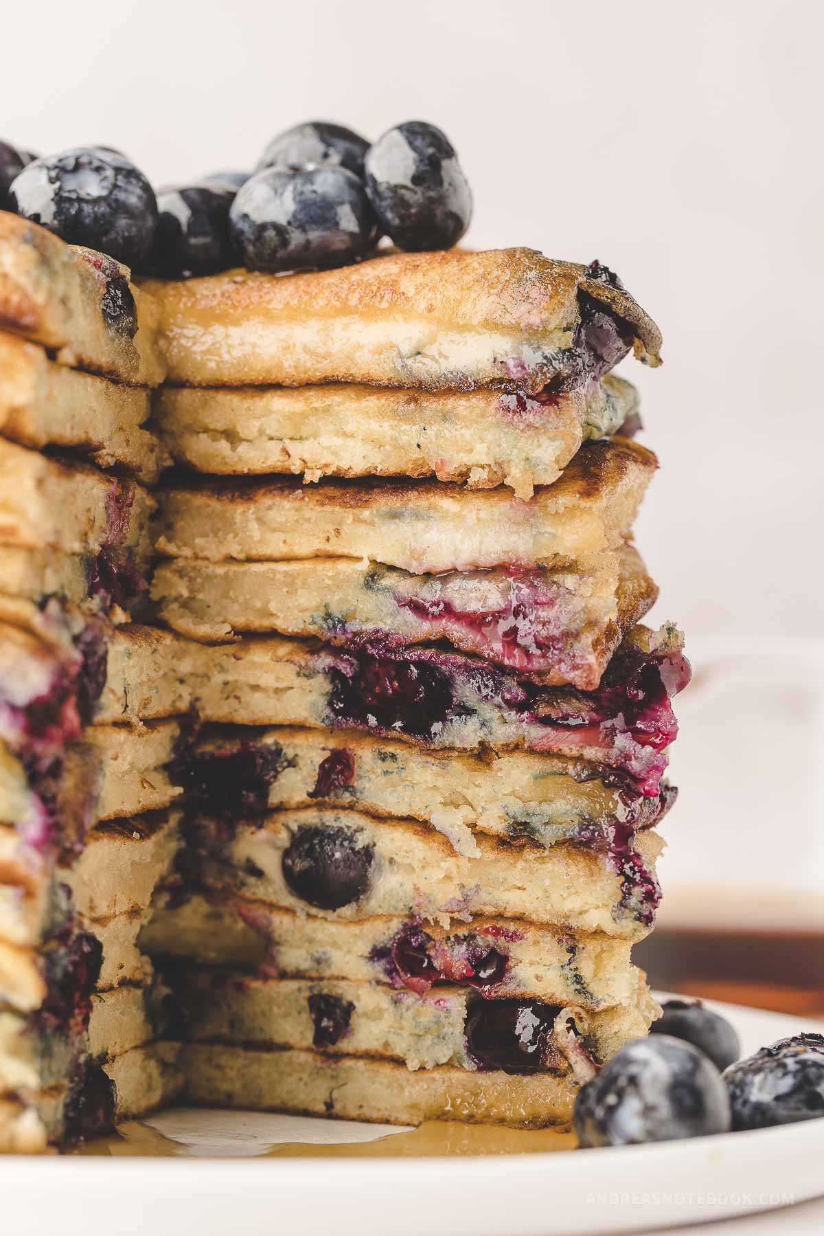 Tall stack of fluffy blueberry pancakes cut open with a pile of fresh blueberries on top.