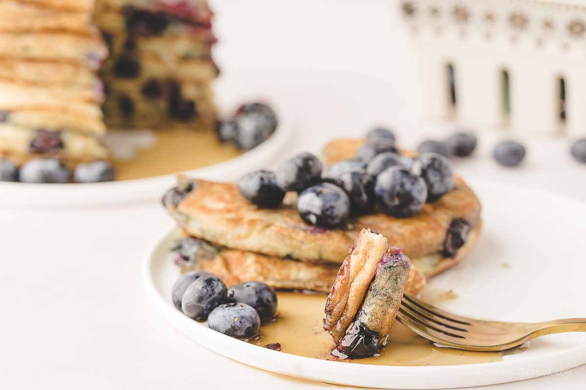 Plate of blueberry pancakes with a bite on a fork.