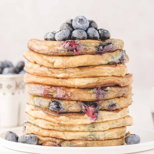 Tall stack of homemade blueberry pancakes with fresh blueberries on top.