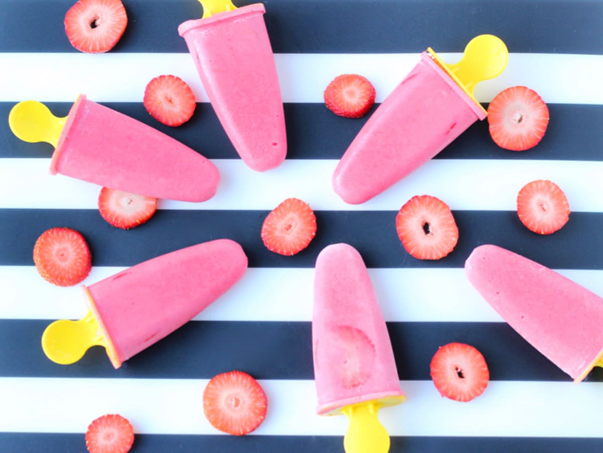 Pink popsicles laying on a blue and white striped placemat with strawberry slices scattered around.