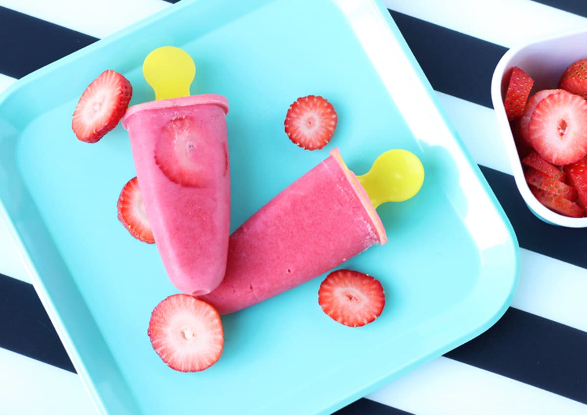Frozen strawberries and cream popsicles on a blue plate.