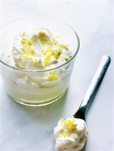 Glass of lemon syllabub dessert with a spoonful lying next to the glass.