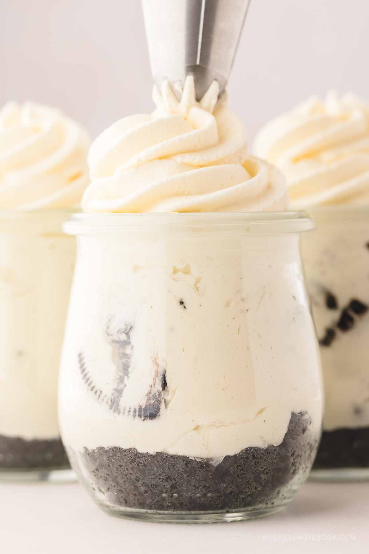 Whipping cream being piped onto the top of an Oreo cheesecake in a jar.