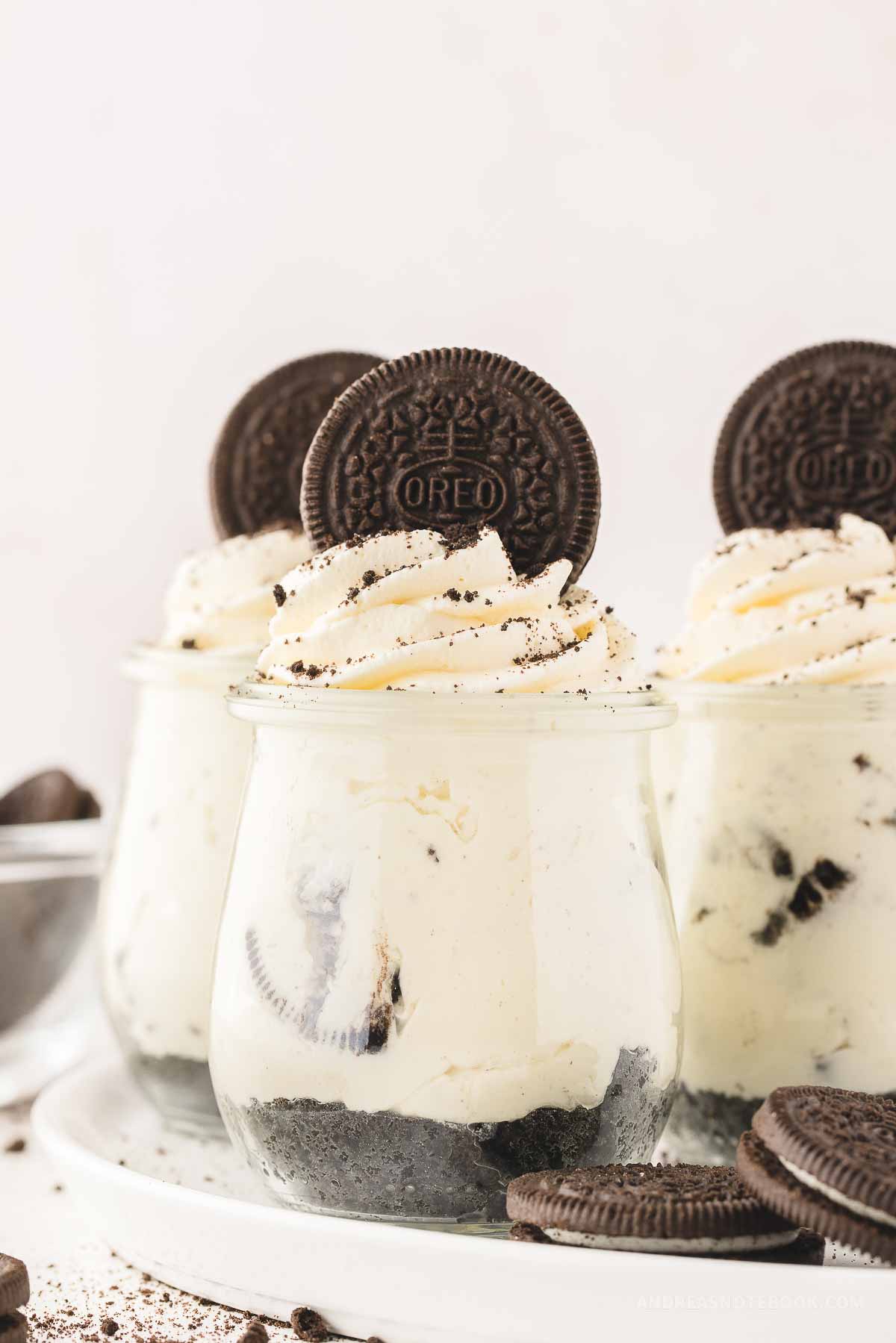 3 jars of oreo cheesecake with a layer of oreo crust, cheesecake and whipped cream with an oreo on top.