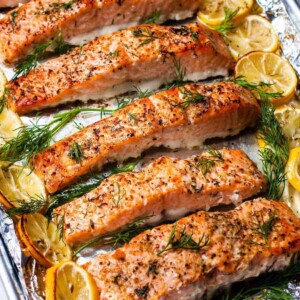 Slices of baked salmon on a baking sheet with lemon slices.