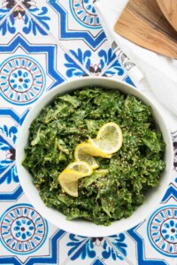 Kale and lemon tahini salad in a white bowl with fresh lemon on top.