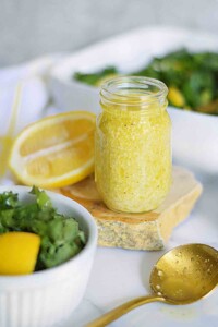 Mason jar full of fresh lemon dressing next to a green salad.