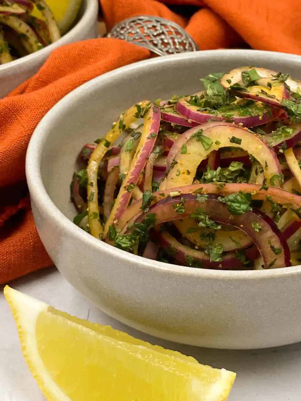 Indian onion salad recipe in a bowl with a slice of lemon.