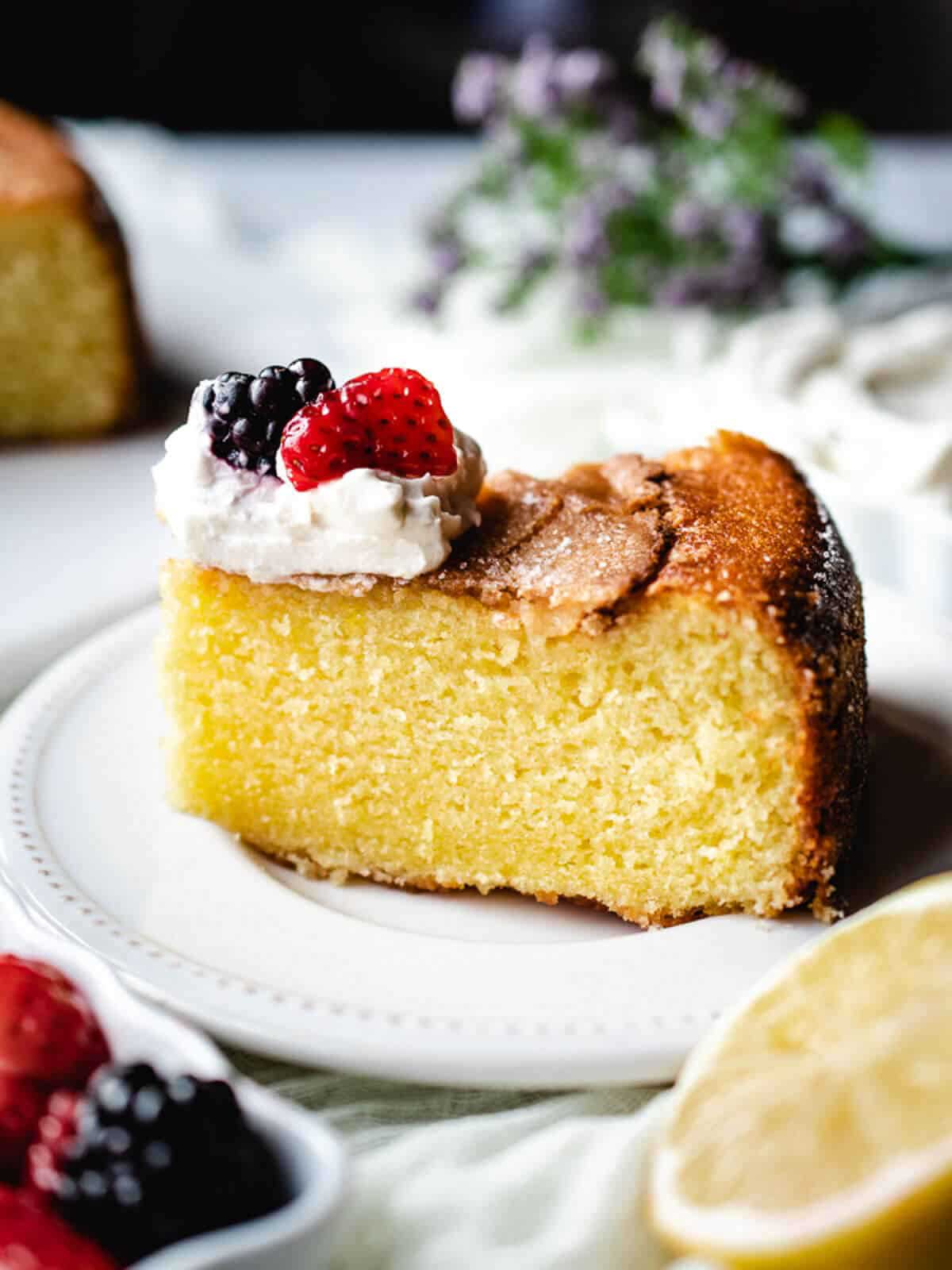 Slice of olive oil lemon cake on a plate with whipped cream and berries on top.
