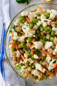 Bowl full of cauliflower salad with carrots and peas.