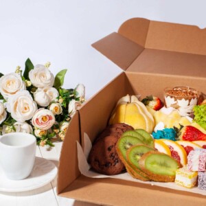 Mini charcuterie box of sweets and fruit next to a bouquet of flowers.